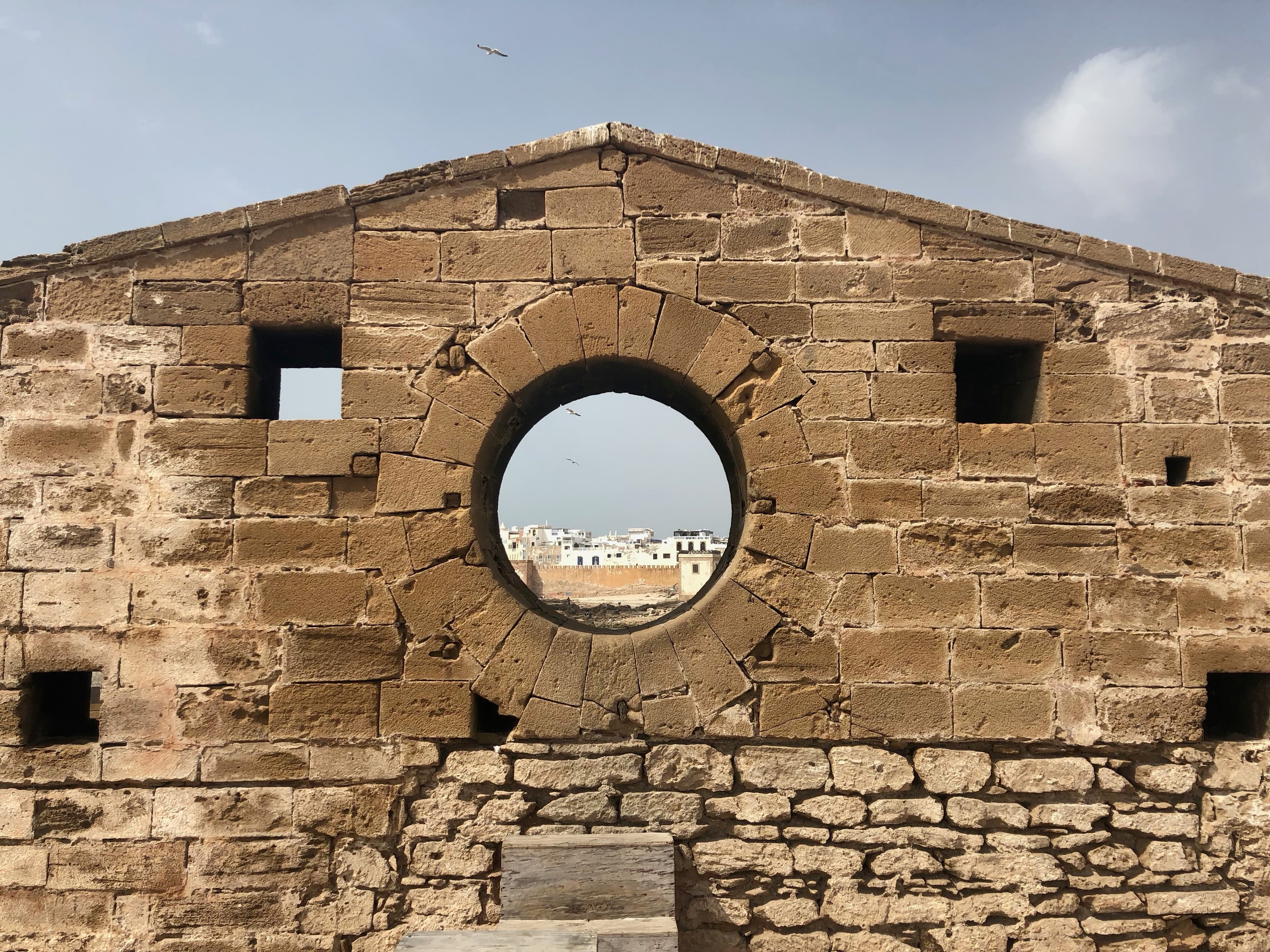 A circular opening in a stone wall frames the white buildings of Essaouira.