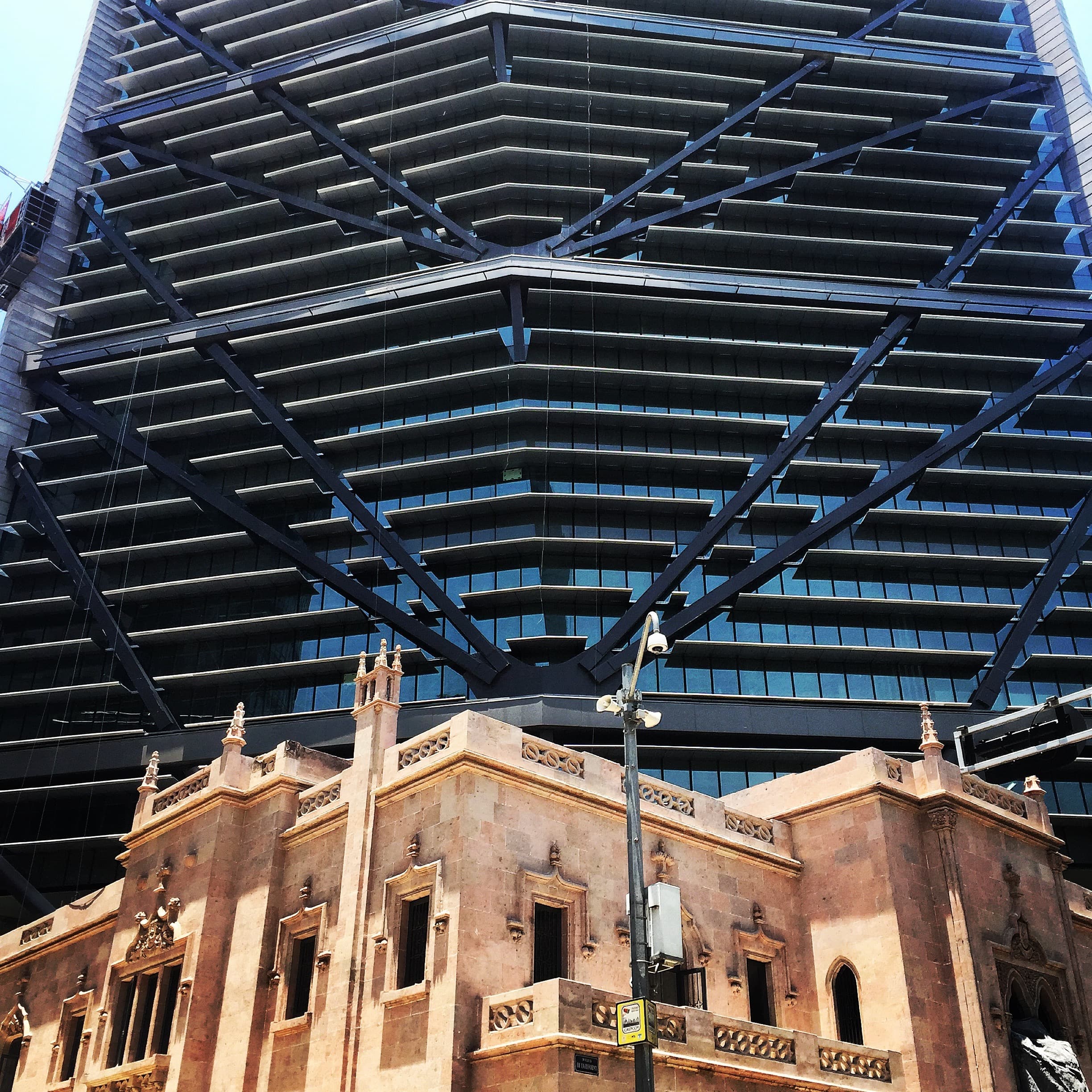 A pink stone building beneath a modern tower with black steel braces.